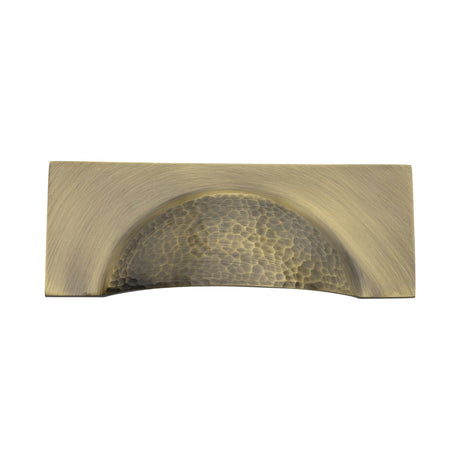 This is an image of a Heritage Brass - Drawer Cup Pull Hampshire Hammered Design 57mm CTC Antique Brass Finish, ham2764-at that is available to order from T.H Wiggans Ironmongery in Kendal.
