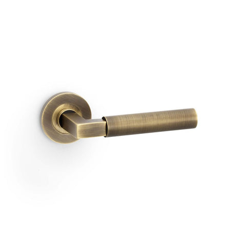 This is an image showing Alexander & Wilks Hurricane Plain Lever on Round Rose - Antique Brass aw201ab available to order from T.H Wiggans Ironmongery in Kendal, quick delivery and discounted prices.