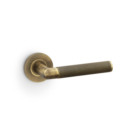 This is an image showing Alexander & Wilks Harrier Knurled Lever on Round Rose - Antique Brass aw210ab available to order from T.H Wiggans Ironmongery in Kendal, quick delivery and discounted prices.