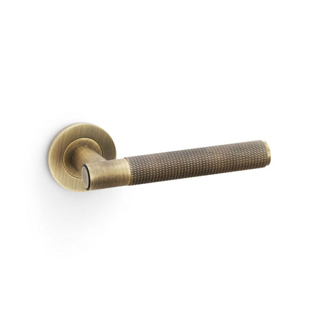 This is an image showing Alexander & Wilks Spitfire Knurled Lever on Round Rose - Antique Brass aw220ab available to order from T.H Wiggans Ironmongery in Kendal, quick delivery and discounted prices.