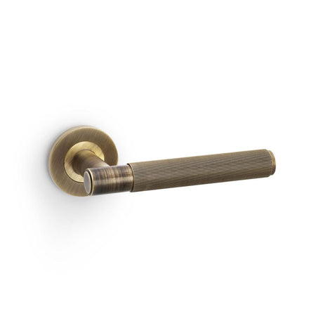This is an image showing Alexander & Wilks Spitfire Reeded Lever on Round Rose - Antique Brass aw222ab available to order from T.H Wiggans Ironmongery in Kendal, quick delivery and discounted prices.