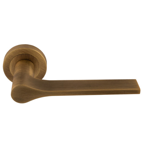 This is an image of a Manital - Vela Lever on Round Rose - Antique Brass vv5ab that is availble to order from T.H Wiggans Ironmongery in Kendal.