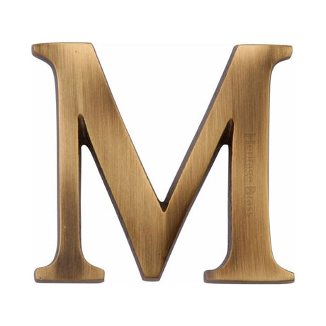 This is an image of a Heritage Brass - Alphabet M Pin Fix 51mm (2") Antique Brass Finish, c1565-2-m-at that is available to order from T.H Wiggans Ironmongery in Kendal.
