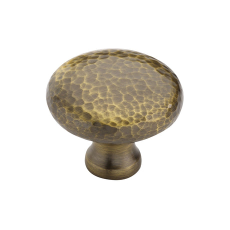 This is an image of a Heritage Brass - Cabinet Knob Victorian Round Hammered Design 38mm Antique Brass finish, ham113-38-at that is available to order from T.H Wiggans Ironmongery in Kendal.