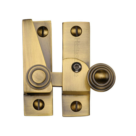 This is an image of a Heritage Brass - Sash Fastener Lockable Antique Brass Finish, v1104l-at that is available to order from T.H Wiggans Ironmongery in Kendal.