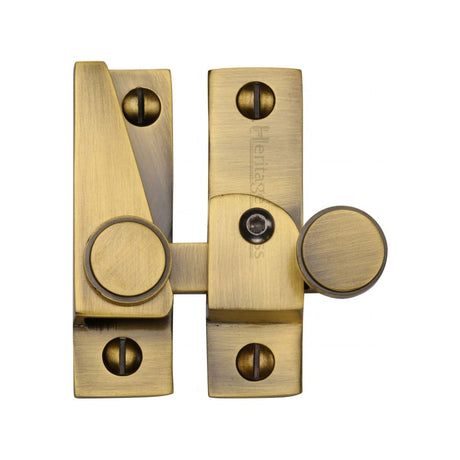 This is an image of a Heritage Brass - Sash Fastener Lockable Antique Brass Finish, v1106l-at that is available to order from T.H Wiggans Ironmongery in Kendal.