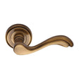 This is an image of a Heritage Brass - Door Handle Lever Latch on Round Rose Lisboa Design Antique Brass, v1601-at that is available to order from T.H Wiggans Ironmongery in Kendal.