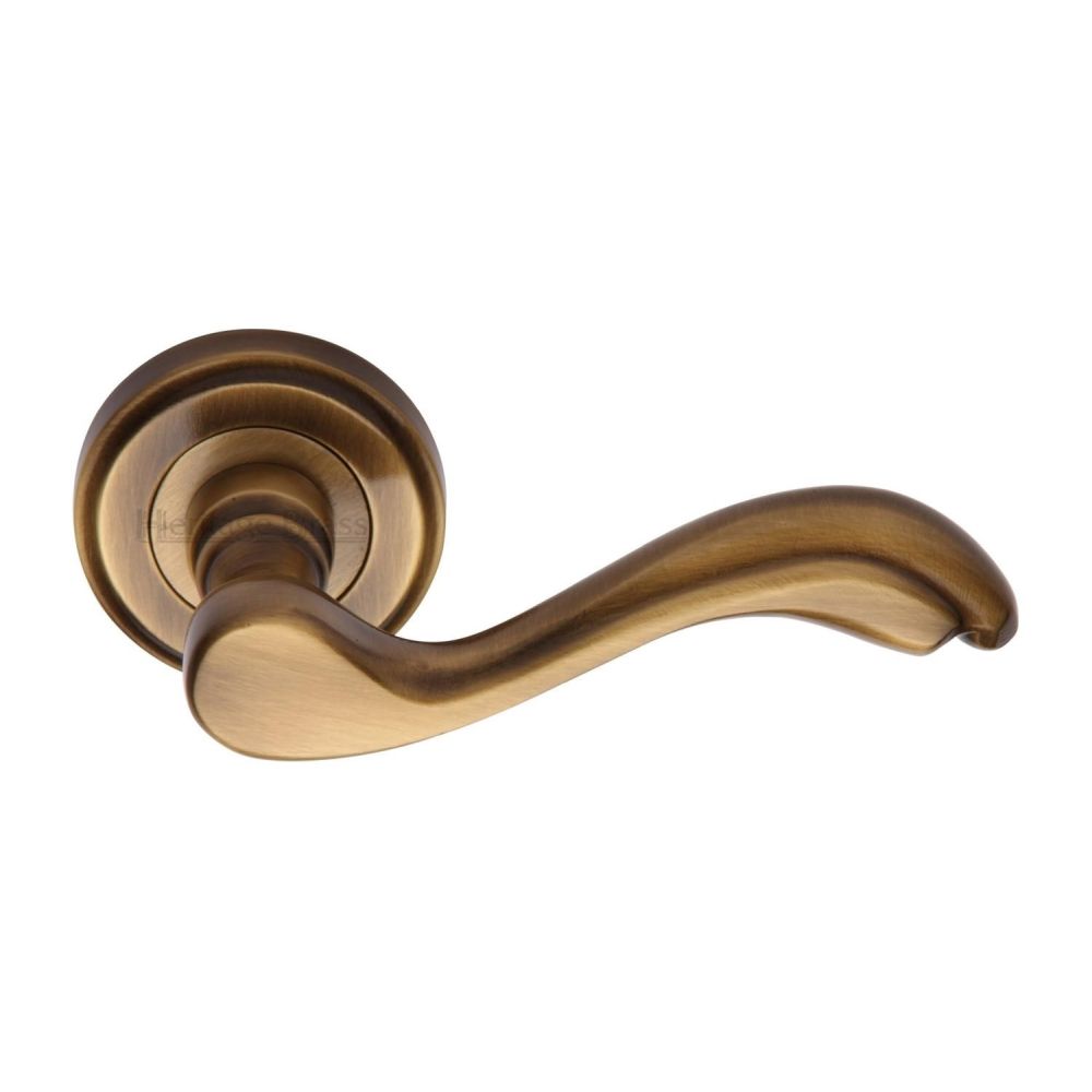This is an image of a Heritage Brass - Door Handle Lever Latch on Round Rose Lisboa Design Antique Brass, v1601-at that is available to order from T.H Wiggans Ironmongery in Kendal.