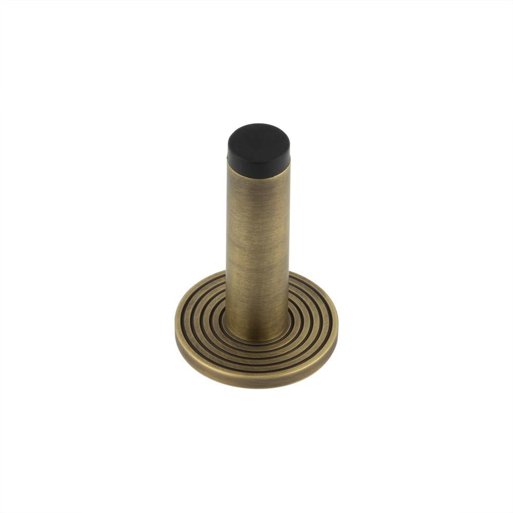 This is an image showing the Frelan - Burlington Plain Wall Mounted Door Stops Reeded Rose Antique Brass available to order from T.H. Wiggans Ironmongery in Kendal