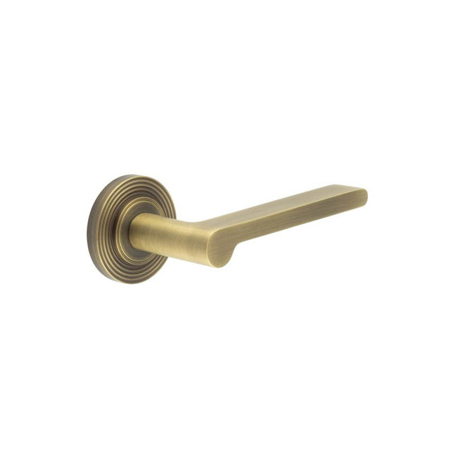 This is an image showing the Frelan - Fitzrovia Door Handles Reeded Rose Antique Brass available to order from T.H. Wiggans Ironmongery in Kendal