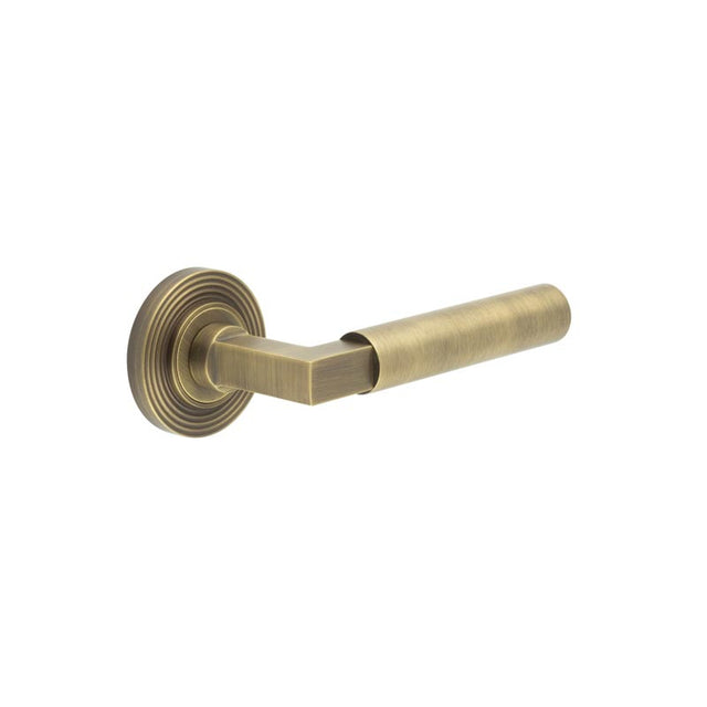 This is an image showing the Frelan - Westminster Door Handle on Reeded Rose Antique Brass available to order from T.H. Wiggans Ironmongery in Kendal