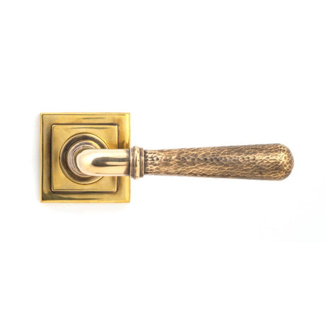 This is an image showing From The Anvil - Aged Brass Hammered Newbury Lever on Rose Set (Square) - Unspru available from trade door handles, quick delivery and discounted prices