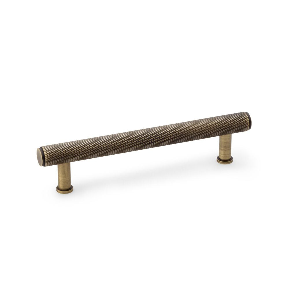 This is an image showing Alexander & Wilks Crispin Knurled T-bar Cupboard Pull Handle - Antique Brass - Centres 128mm aw809-128-ab available to order from T.H Wiggans Ironmongery in Kendal, quick delivery and discounted prices.