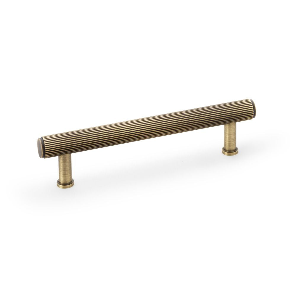 This is an image showing Alexander & Wilks Crispin Reeded T-bar Cupboard Pull Handle - Antique Brass - 128mm aw809r-128-ab available to order from T.H Wiggans Ironmongery in Kendal, quick delivery and discounted prices.