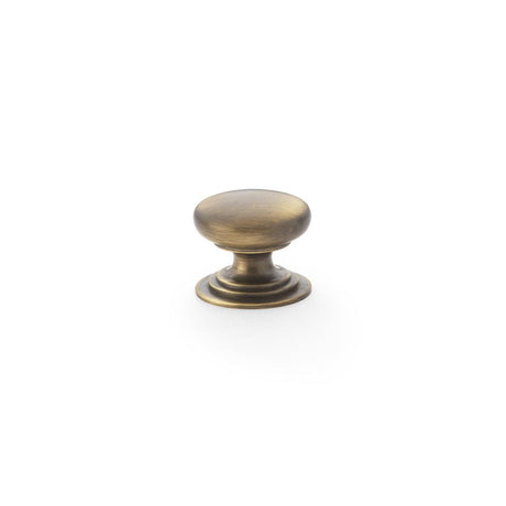 This is an image showing Alexander & Wilks Waltz Round Cupboard Knob on Stepped Rose - Antique Brass - 25mm aw825-25-ab available to order from T.H Wiggans Ironmongery in Kendal, quick delivery and discounted prices.