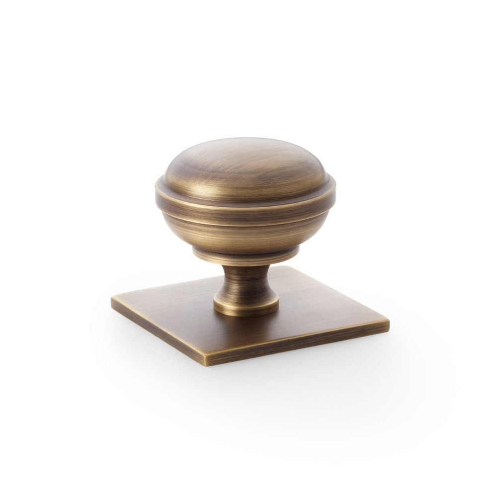 This is an image showing Alexander & Wilks Quantock Cupboard Knob on Square Backplate - Antique Brass - 38mm aw826-38-ab available to order from T.H Wiggans Ironmongery in Kendal, quick delivery and discounted prices.