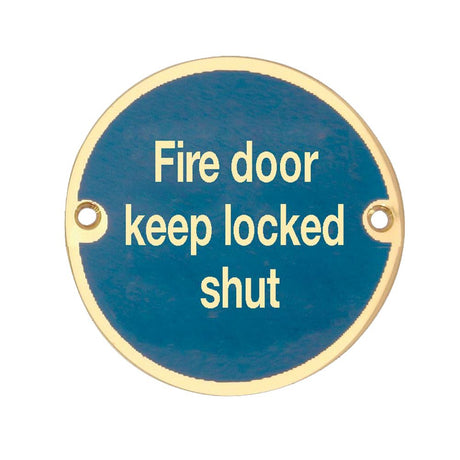 This is an image showing the Frelan - Fire Door Keep Locked Shut - Signage 75mm Dia. - Polished Brass available to order from T.H. Wiggans Ironmongery in Kendal